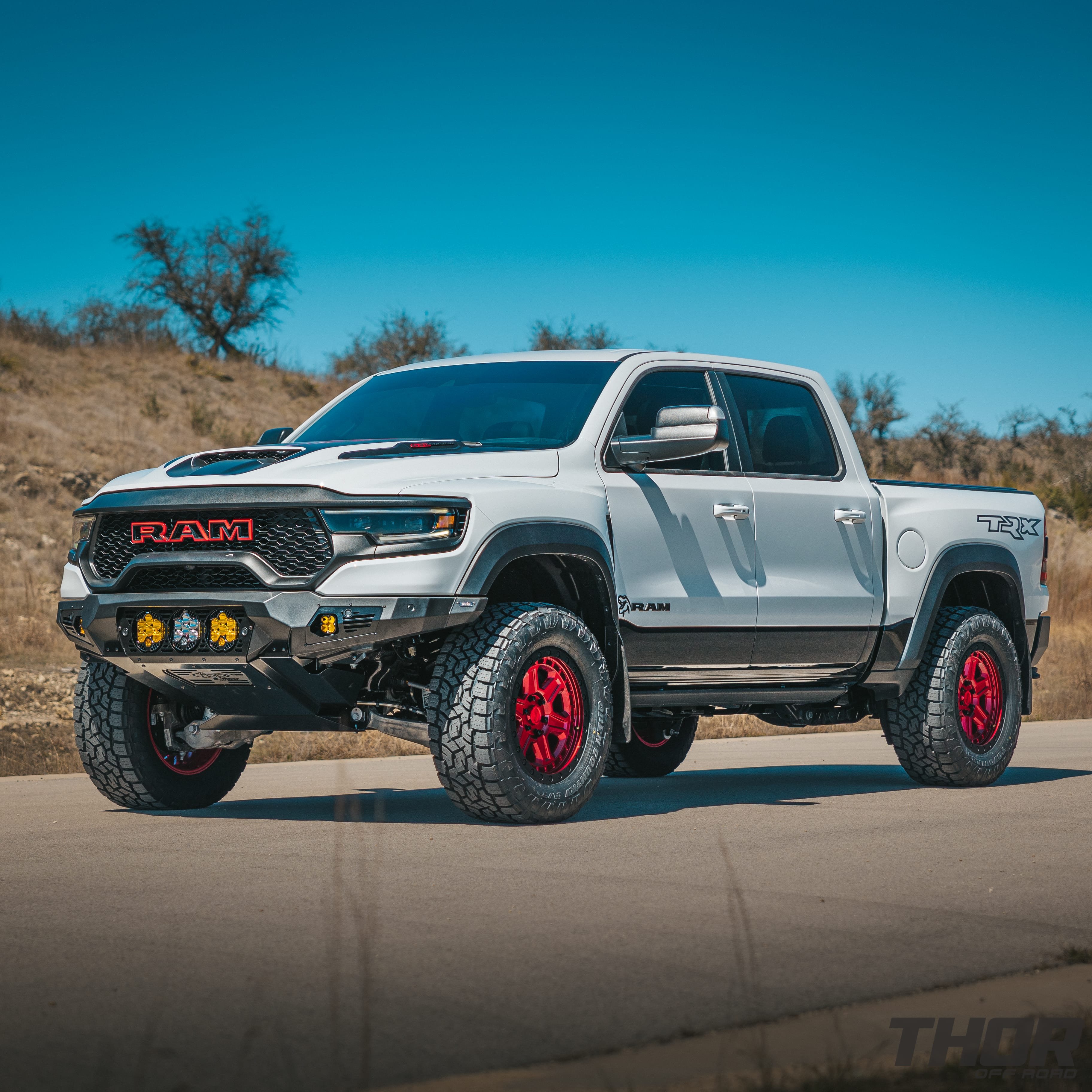 2022 RAM 1500 TRX in White with AFE Leveling Kit, 20x9" Black Rhino Reno Candy Red Wheels, 35x12.50R20 Toyo AT III, ADD Front and Rear Bumpers, Baja Design LP6 Center Lights, Baja Design Squadron Front and Rear Lights, Retrax Pro MX Bed Cover, Baja Design Rock Lighting
