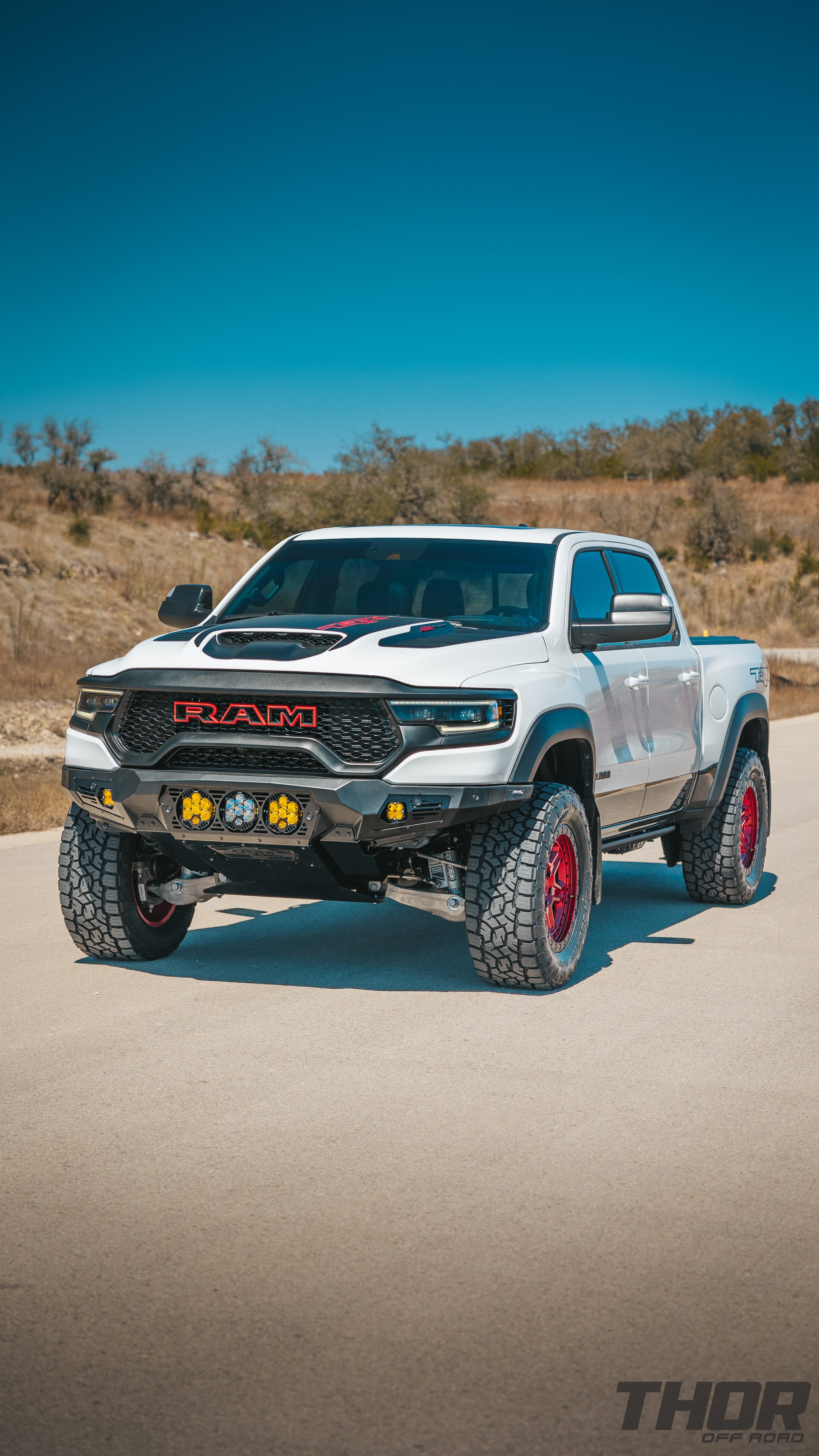 2022 RAM 1500 TRX in White with AFE Leveling Kit, 20x9" Black Rhino Reno Candy Red Wheels, 35x12.50R20 Toyo AT III, ADD Front and Rear Bumpers, Baja Design LP6 Center Lights, Baja Design Squadron Front and Rear Lights, Retrax Pro MX Bed Cover, Baja Design Rock Lighting