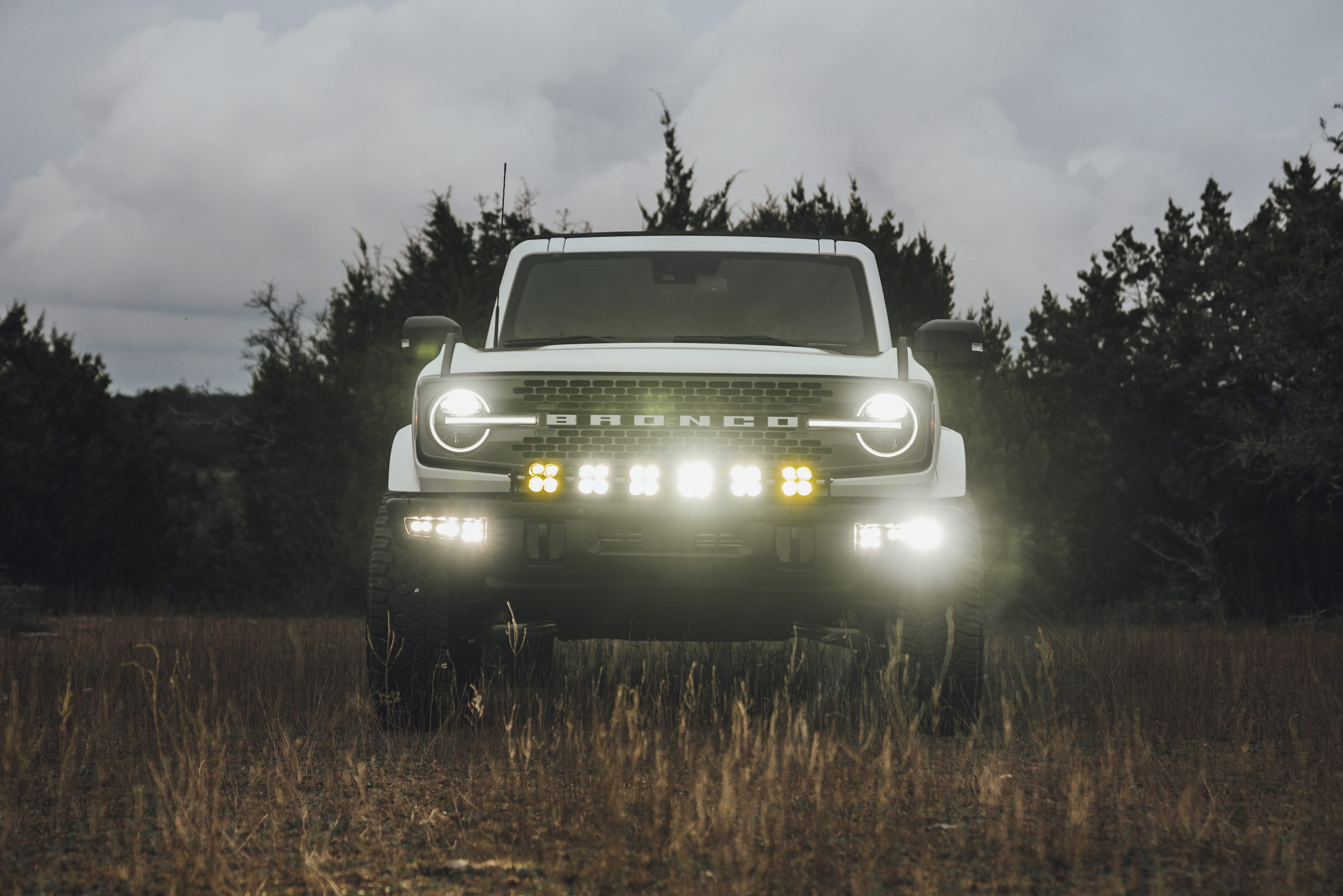 2021 Ford Bronco Badlands in Oxford White with Baja Design Fog Light Pocket Kit, XL Squadron Sport Linkable Lights, 17" Raceline wheels, 35x12.50R17 Yokohama Geolander X-AT Tires, Rough Country Spare Tire Extender, Third Brake Light Relocation Bracket, Paint Matched Fender Flares, Retro Striping, Retro Badges