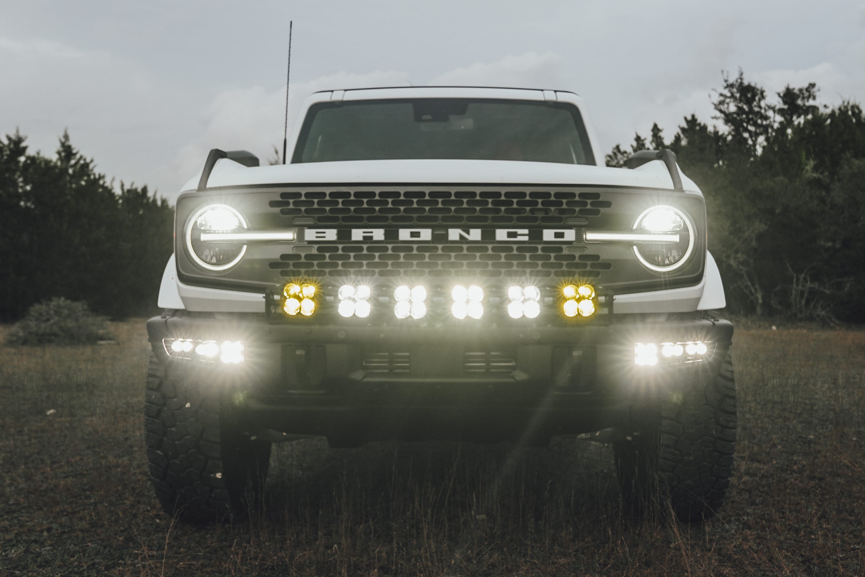 2021 Ford Bronco Badlands in Oxford White with Baja Design Fog Light Pocket Kit, XL Squadron Sport Linkable Lights, 17" Raceline wheels, 35x12.50R17 Yokohama Geolander X-AT Tires, Rough Country Spare Tire Extender, Third Brake Light Relocation Bracket, Paint Matched Fender Flares, Retro Striping, Retro Badges