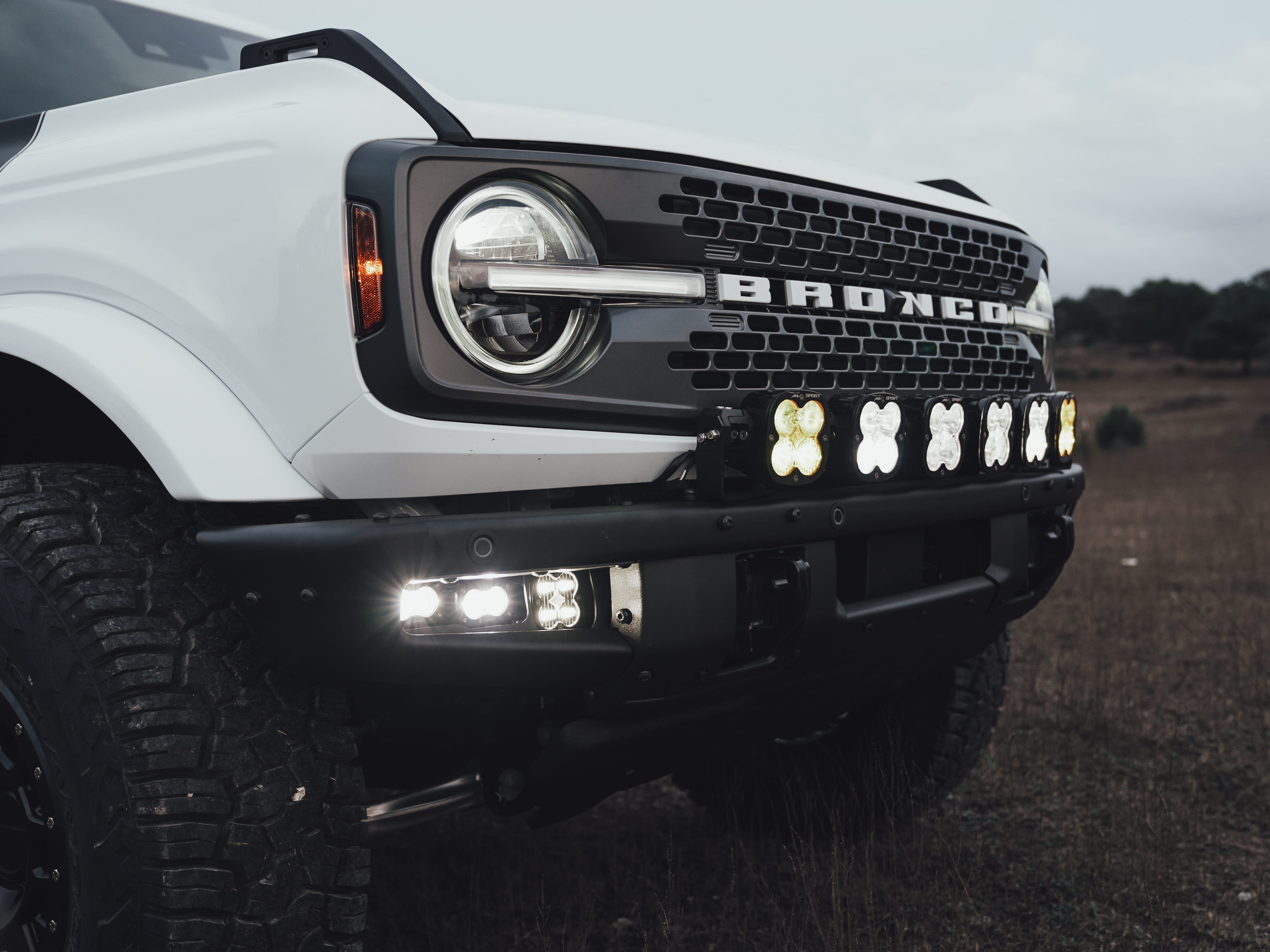 2021 Ford Bronco Badlands in Oxford White with Baja Design Fog Light Pocket Kit, XL Squadron Sport Linkable Lights, 17" Raceline wheels, 35x12.50R17 Yokohama Geolander X-AT Tires, Rough Country Spare Tire Extender, Third Brake Light Relocation Bracket, Paint Matched Fender Flares, Retro Striping, Retro Badges