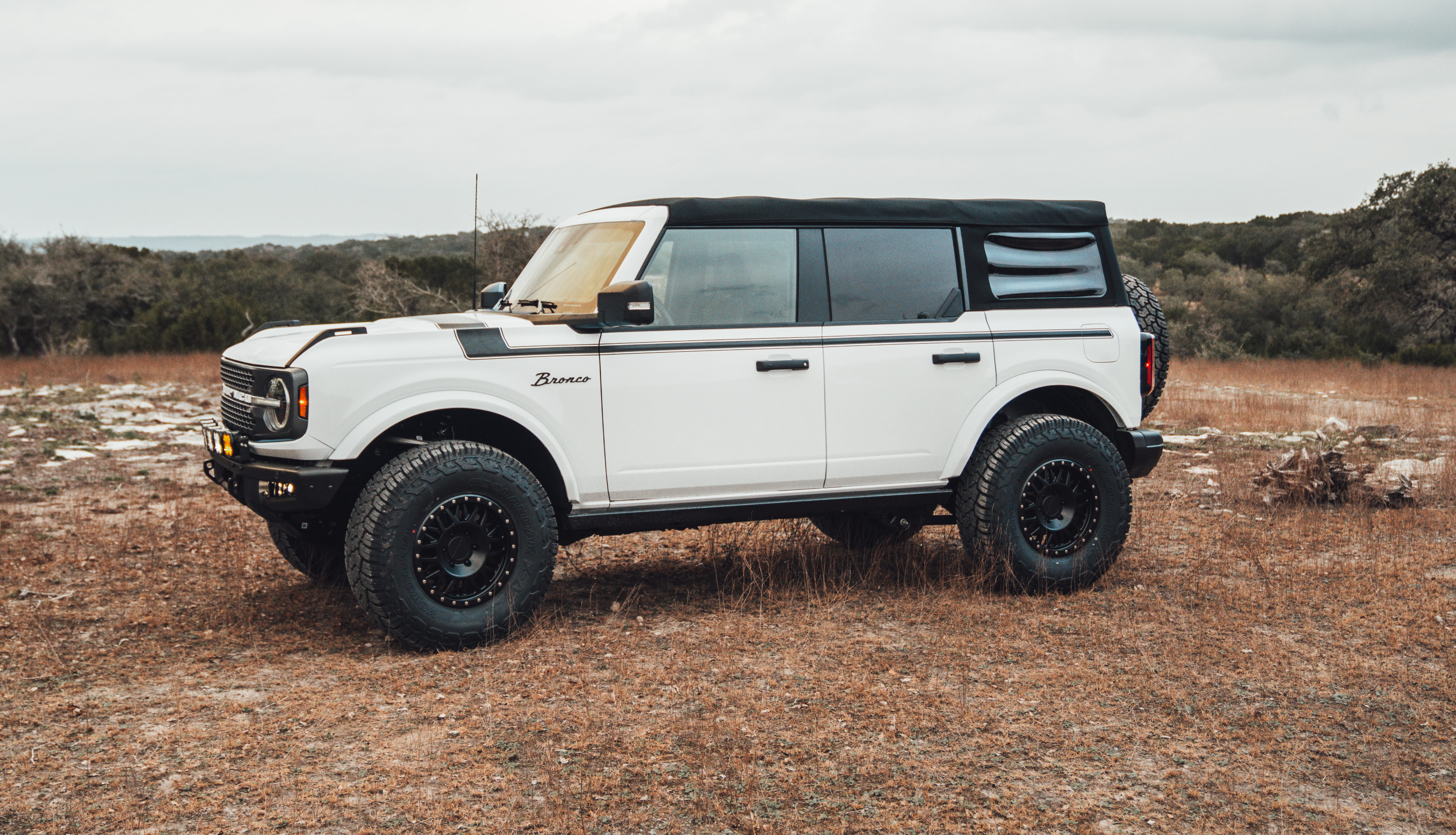 2021 Ford Bronco Badlands in Oxford White with Baja Design Fog Light Pocket Kit, XL Squadron Sport Linkable Lights, 17" Raceline wheels, 35x12.50R17 Yokohama Geolander X-AT Tires, Rough Country Spare Tire Extender, Third Brake Light Relocation Bracket, Paint Matched Fender Flares, Retro Striping, Retro Badges