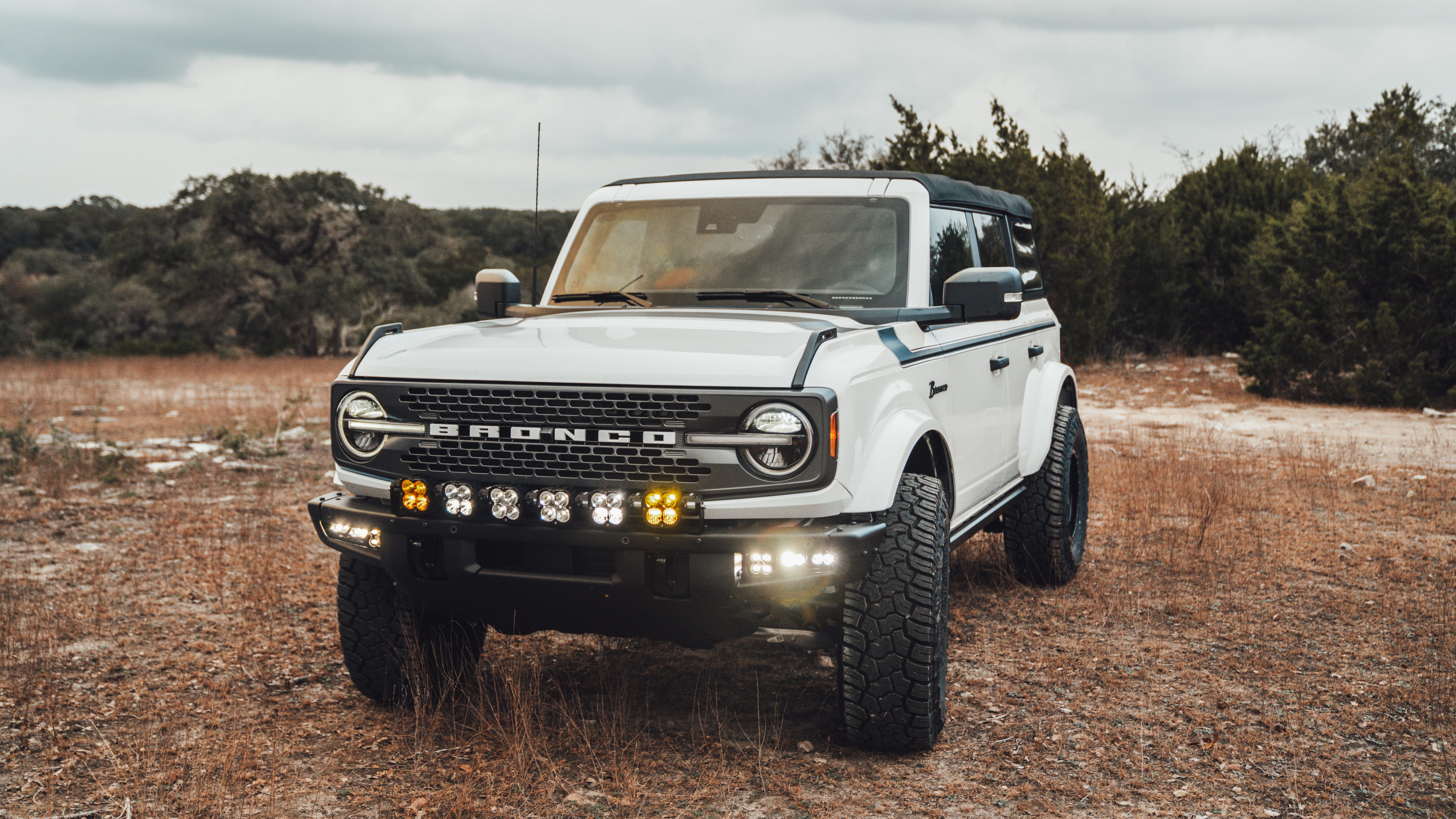 2021 Ford Bronco Badlands in Oxford White with Baja Design Fog Light Pocket Kit, XL Squadron Sport Linkable Lights, 17" Raceline wheels, 35x12.50R17 Yokohama Geolander X-AT Tires, Rough Country Spare Tire Extender, Third Brake Light Relocation Bracket, Paint Matched Fender Flares, Retro Striping, Retro Badges