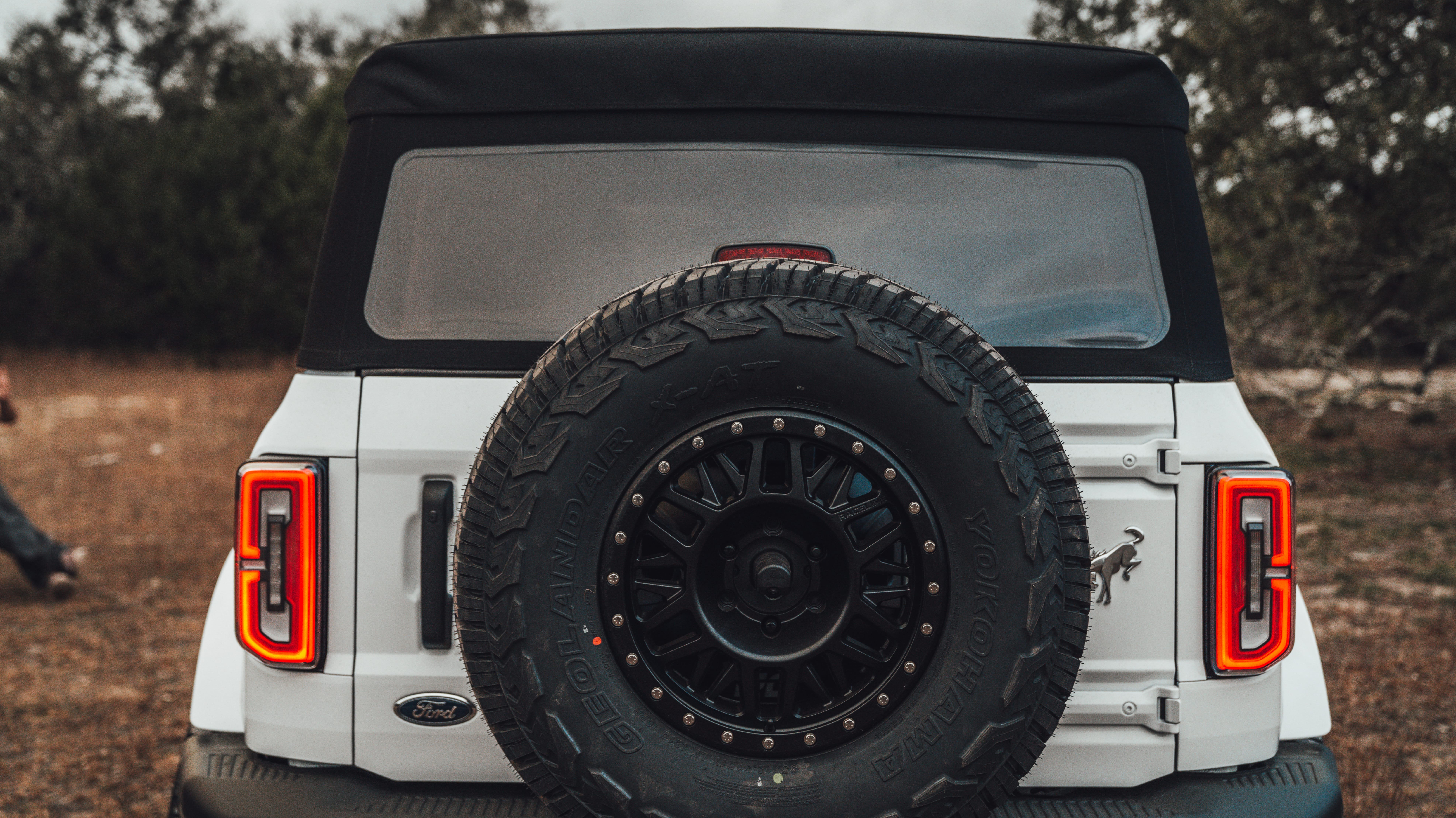 2021 Ford Bronco Badlands in Oxford White with Baja Design Fog Light Pocket Kit, XL Squadron Sport Linkable Lights, 17" Raceline wheels, 35x12.50R17 Yokohama Geolander X-AT Tires, Rough Country Spare Tire Extender, Third Brake Light Relocation Bracket, Paint Matched Fender Flares, Retro Striping, Retro Badges