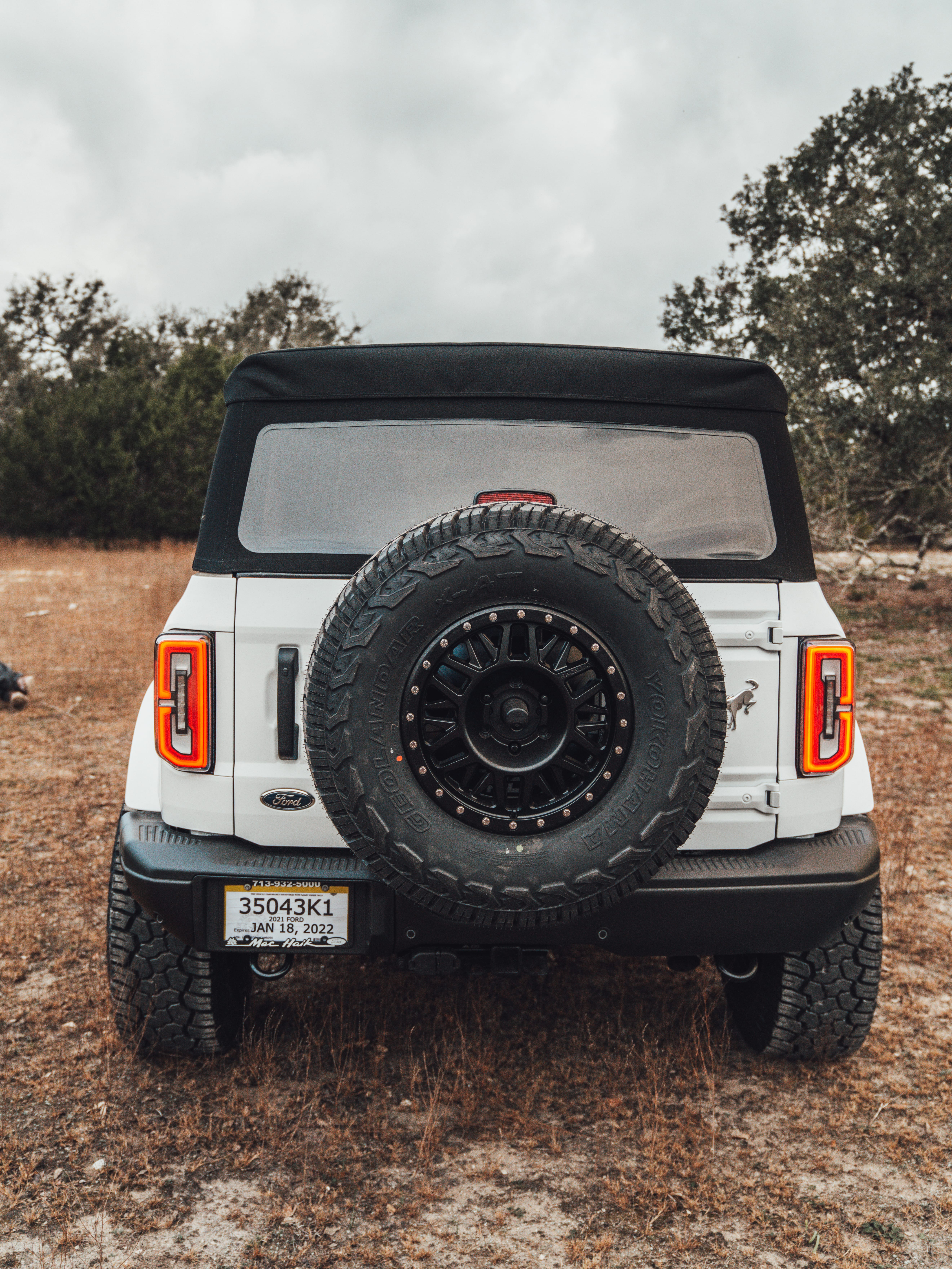 2021 Ford Bronco Badlands in Oxford White with Baja Design Fog Light Pocket Kit, XL Squadron Sport Linkable Lights, 17" Raceline wheels, 35x12.50R17 Yokohama Geolander X-AT Tires, Rough Country Spare Tire Extender, Third Brake Light Relocation Bracket, Paint Matched Fender Flares, Retro Striping, Retro Badges