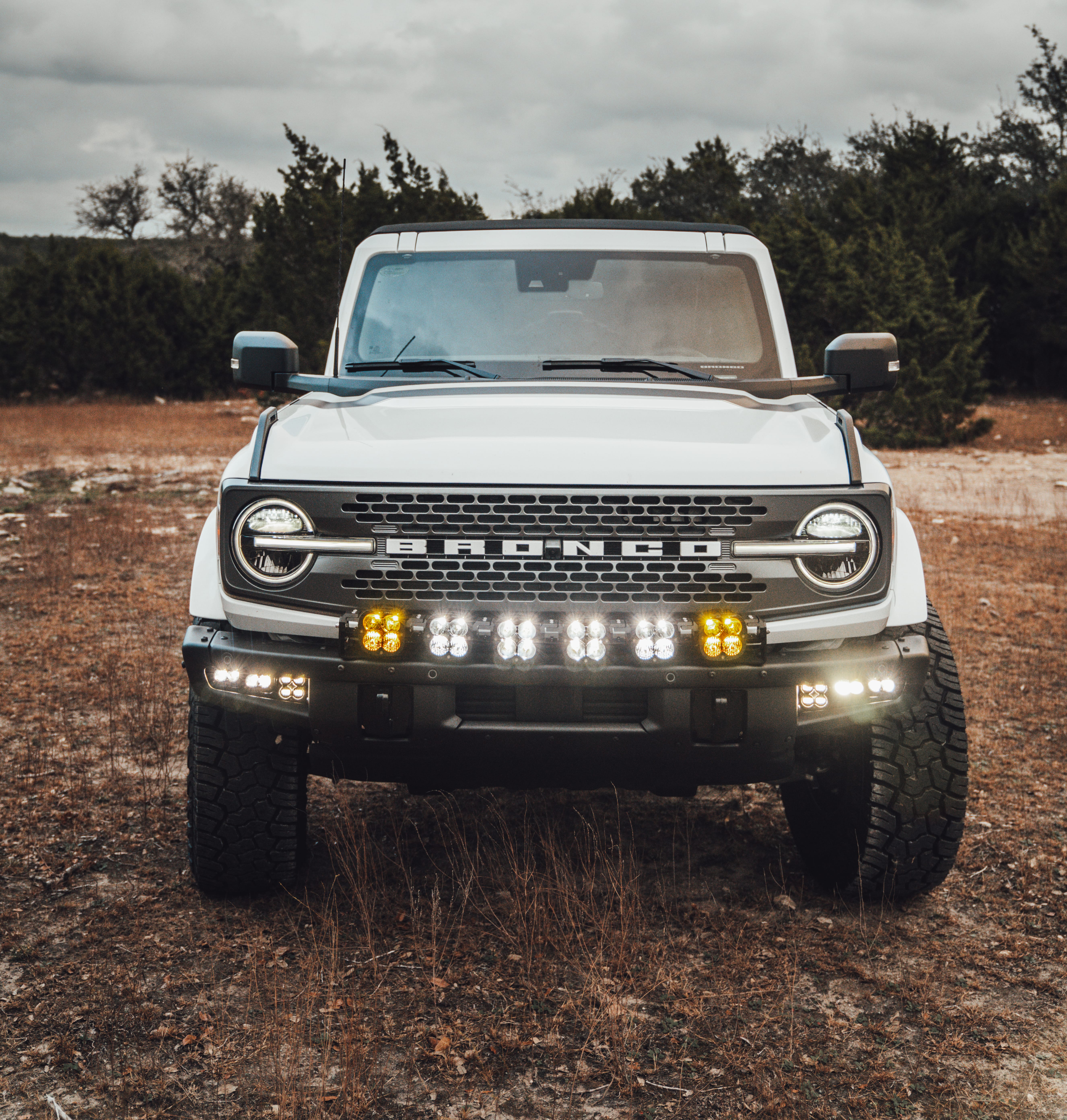 2021 Ford Bronco Badlands in Oxford White with Baja Design Fog Light Pocket Kit, XL Squadron Sport Linkable Lights, 17" Raceline wheels, 35x12.50R17 Yokohama Geolander X-AT Tires, Rough Country Spare Tire Extender, Third Brake Light Relocation Bracket, Paint Matched Fender Flares, Retro Striping, Retro Badges