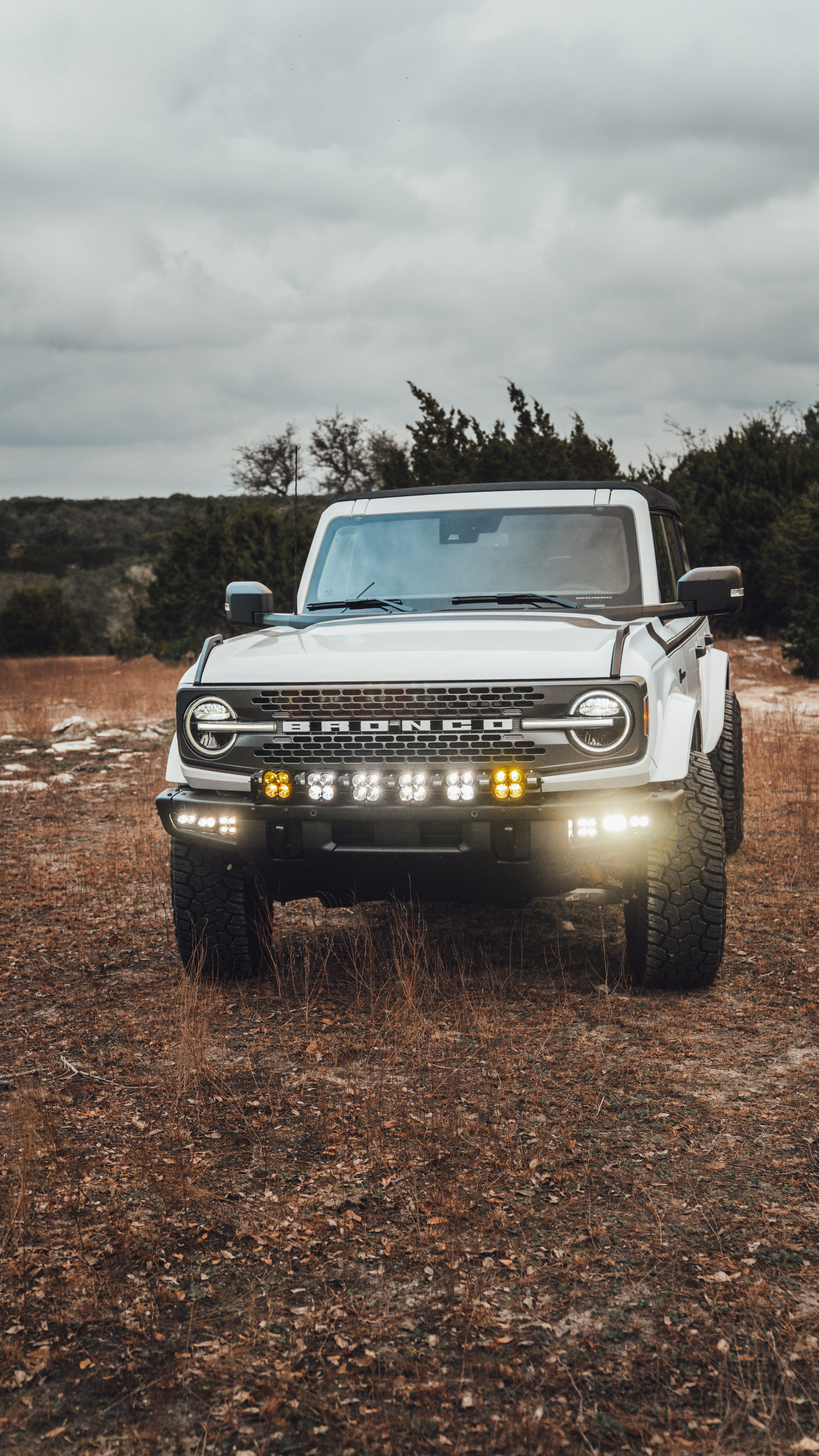 2021 Ford Bronco Badlands in Oxford White with Baja Design Fog Light Pocket Kit, XL Squadron Sport Linkable Lights, 17" Raceline wheels, 35x12.50R17 Yokohama Geolander X-AT Tires, Rough Country Spare Tire Extender, Third Brake Light Relocation Bracket, Paint Matched Fender Flares, Retro Striping, Retro Badges